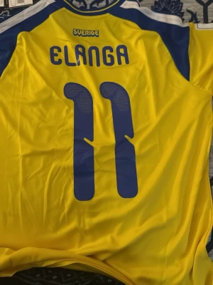 Sverige matchtröja Elanga #11 Helt ny med prislappen. - Gul och blå matchtröja från Sveriges landslag med Elanga och nummer 11 på ryggen. Tröjan har korta ärmar, blå detaljer på axlar och ärmar samt landslagets emblem på bröstet. Tillverkad i lätt och ventilerande material, perfekt för och ha i kommande EM