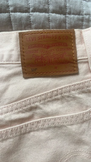 Ljusrosa jeansshorts från Levi's - Säljer ett par ljusrosa jeansshorts från Levi's 501 med rå kant nertill och klassiska bakfickor. Shortsen har hög midja och är tillverkade i bomull, perfekta för sommaren. Dom är korta i benen och höga i midjan och bekväma. Använt en gång. 