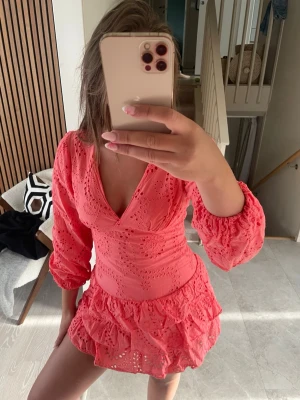 Korallfärgad klänning med volang - Supersöt kort klänning i korall med broderade detaljer och volangkant. Klänningen har v-ringning och är från meet me there! Den är helt ny och oanvänd och kommer med prislapp. 