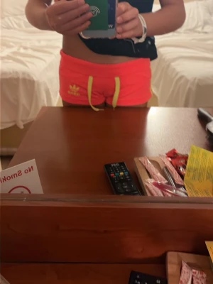 Neonrosa Adidas shorts med snörning - Säljer ett par korall Adidas shorts med gula detaljer och snörning i midjan. Shortsen har tre gula ränder på sidan och Adidas-logga framtill. Perfekta för sommarens alla aktiviteter!