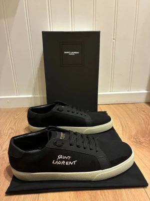 Saint Laurent canvas sneakers - Svarta sneakers från Saint Laurent med vit sula och handskriven logga på sidan. Skorna har klassisk låg profil, svarta skosnören och detaljer i textil och läder. Perfekta för en clean och stilren look.