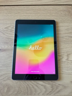 Apple iPad 6th gen - Säljer en Apple iPad med svart ram och silverfärgad baksida. Surfplattan har en stor skärm med hemknapp och Apples logga på baksidan. Perfekt för surf, spel och streaming. Modern design i aluminium och glas. Inga skador. 128gb