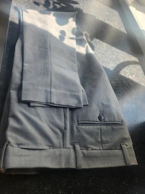 Grå kostymbyxor med pressveck jack and jones. Storlek 29/ 30 - Snygga grå kostymbyxor med klassiskt pressveck och uppvikta benslut. Byxorna har bakficka med knapp och bälteshällor. Perfekta för en stilren och modern look. Storlek 29/30