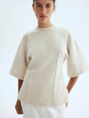Beige topp med vida ärmar - Säljer en stilren beige topp med rund hals och vida, halvlånga ärmar. Toppen har en lätt strukturerad yta och markerade sömmar framtill som ger en modern look. Perfekt att matcha med både jeans och kjol för en clean stil.
