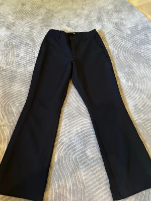 Svarta utsvängda kostymbyxor - Snygga svarta kostymbyxor med utsvängda ben och hög midja. Klassisk design med bälteshällor och fickor fram. Perfekta för en stilren och trendig look. 