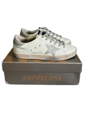 Golden Goose - Golden Goose Superstar sneakers i vitt skinn med silverglittrig stjärna på sidan och silverdetaljer på hälen. Grå snörning och platt sula. Klassisk låg modell med svart GGDB-märke på plösen. Perfekta för dig som gillar en clean men ändå glittrig look. Storlek 39 passar även 40🤝 använda 1 gång