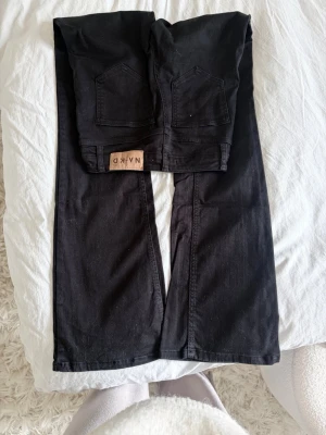 Svarta flared jeans från NA-KD - Säljer ett par svarta jeans från NA-KD med flared passform och hög midja. Jeansen har klassiska fem fickor, silverfärgade knappar och en patch med logga bak. Materialet är kraftigt denim som ger en snygg siluett.  Obs jeansen är helsvarta, blev bara konstigt ljus på bilden.