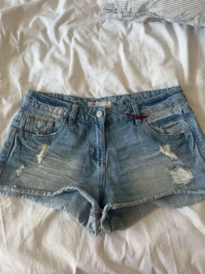 Ljusblå slitna jeansshorts - Säljer ett par ljusblå jeansshorts med slitna detaljer. Säljer pågrund av att dem inte kommer till användning 