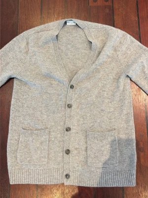 John Henric cardigan - Grå Kashmir kofta med v-ringning och knäppning framtill. Koftan har två framfickor och ribbade muddar vid ärmslut och nederkant. Perfekt för lager på lager och enkel att matcha med olika outfits. Pris kan diskuteras.