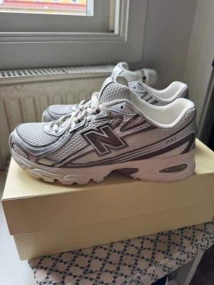 New Balance 740 vita sneakers - Stilrena vita New Balance 740 sneakers med mesh- och syntetmaterial. Skorna har silvriga och grå detaljer samt den klassiska N-loggan på sidan. Lågt skaft och bekväm sula för en sportig look. Inget täcken på slitage eller användning, storleken är 38.5. 