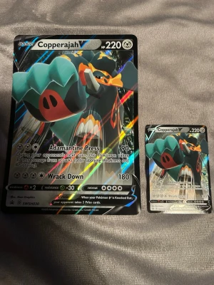 Pokémonkort Copperajah V jumbo & vanlig - Två Pokémonkort av Copperajah V, ett i jumboformat och ett i standardstorlek. Båda har en glansig yta med färgstark design och visar Copperajah i en dynamisk pose. Perfekt för samlare eller Pokémon-fans som vill utöka sin kortsamling.