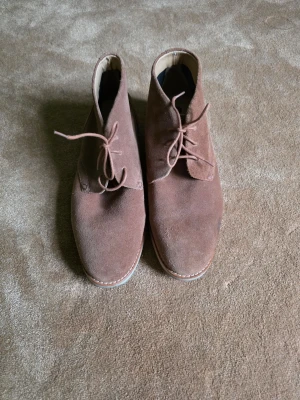 Bruna mocka chukka boots - Snygga bruna chukka boots i mocka med klassisk snörning och låg profil. Skorna har en ljus sula och stilren design som passar perfekt till jeans eller chinos. Materialet är mjukt och ger en avslappnad men ändå uppklädd känsla. Använda enstaka gång. 