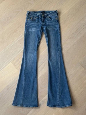 True religion jeans - Säljer ett par blåa true religion jeans med låg midja och snygga fickdetaljer bak. Dom är i bra skick men har ett litet hål längst ner på vänster ben och är lite slitna även längst ner  på höger ben.