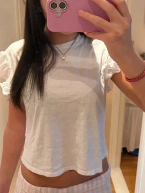 Vit croppad topp med volangärmar - Söt vit croppad topp med korta volangärmar. Toppen har en avslappnad passform och är tillverkad i mjuk bomull, perfekt för en chill och trendig look. Enkel att matcha med både jeans och kjol.