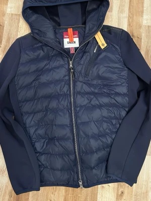 Mörkblå parajumper cardigan - Säljer för denna fina parajumper cardigan i mörkblå. Storlek S och passar perfekt för er som är 170cm och uppåt. Funkar också för er som är 165 skulle jag nog tro också. Den är i mycket bra skick. Inga skador eller så. Den har många fickor vilket är bra att ha. Bröst ficka, två inne fickor, 2 vanliga fickor och en ficka på nedersta delen av ryggen. Skriv om ni är intresserade. 