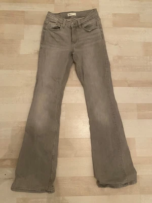 Grå bootcut jeans med hög midja - Säljer ett par gråa bootcut jeans med hög midja och klassiska fem fickor. Jeansen har utsvängda ben och är tillverkade i ett mjukt denimtyg. Perfekta för en avslappnad och trendig look.