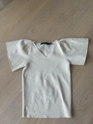 Krämvit topp - Säljer en v-ringad och krämvit topp från Bikbok. Den har puffärmar och lite tjockare ribbat material, den är i storlek M men passar även S och kanske XS då den är lite mindre i storlek. Knappt använd.