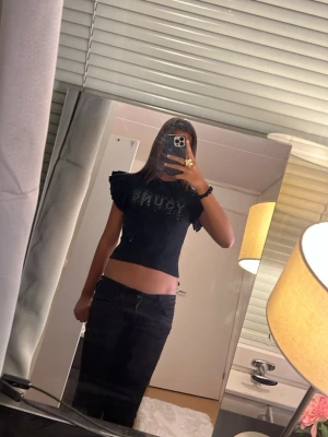 Svart topp med volangärmar och strass - Snygg svart topp med texten 'YOUNG' i glittrande strass framtill. Toppen har korta volangarmar.