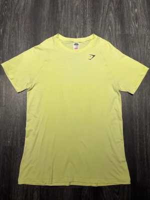 Gymshark Vital Seamless tränings T-shirt 2018 - Fräsch Gymshark-träningströja i en snygg limegul nyans. Äldre Vital Seamless-modell med ventilerande detaljer och Muscle Fit-passform som framhäver fysiken och sitter snyggt över bröst, axlar och armar. Tröjan är i exceptionellt fint skick, nästintill aldrig använd och helt utan skador eller slitage. Väldigt välbevarad och känns fortfarande som ny. Perfekt för gym och träning.