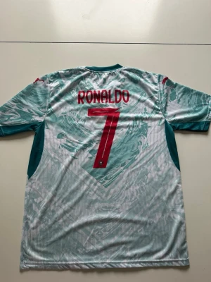 Portugal Ronaldo matchtröja nr 7 - Säljer en Portugal fotbollströja med Ronaldo och nummer 7 på ryggen. Tröjan är vit med ljusgröna mönster och röda detaljer, samt Portugal-emblemet på bröstet. Tillverkad i lätt och ventilerande material, perfekt för träning eller match. Kan diskutera pris vid snabb affär!