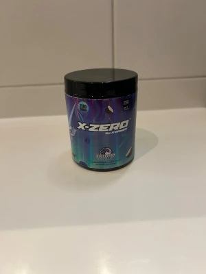 X-Zero Blueberry Coconut pulver - Burk med X-Zero sockerfritt pulver i smaken Blueberry Coconut. Förpackningen är blå-lila med svart lock och har futuristisk design. Perfekt för dig som vill ha en smakrik dryck utan socker.