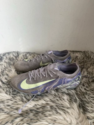Lila Nike löparspikskor - Säljer ett par lila Nike löparspikskor med limegröna detaljer och stor Swoosh på sidan. Skorna har snörning, låg profil och genomskinlig sula med spikar för bra grepp på banan. Perfekta för friidrott och sprint. Med en liten uppfräschning är de i riktigt bra skick!