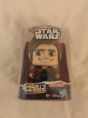Leksak sammlarobjekt Star Wars Mighty Muggs - Han Solo - Star Wars Mighty Muggs samlarfigur, föreställande karaktären Han Solo.  Figuren tillverkas av Hasbro och Disney.  Det unika med den här leksaken är dess inbyggda mekanism.  När du trycker ner den lilla röda knappen på toppen av plastförpackningen (eller trycker på figurens huvud om den är utpackad) så snurrar huvudet.   Figuren har totalt tre olika ansiktsuttryck som visar olika känslor och humör.  Informatio om produkten:   Karaktär: Han Solo (#10 i serien)  Tillverkare: Hasbro  Rekommenderad å
