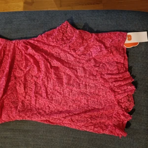 Axelbandslös klänning, oanvänd  - Oanvänd, prislapp kvar. Ca 65cm lång, ca 40cm över bysten. Tre lager tyg, överst två lager genomskinlig spets, underst tyg enligt bild.