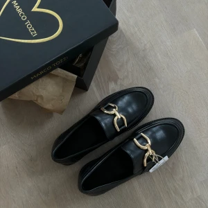 Klassiska chic loafers i skinnimitation MARCO TOZZI - Oanvända stilrena loafers som tyvärr måste säljas pga lite fel storlek/passform för mig. Mycket bekväma dock och fin kvalitet. Med original skokartong. True to size.