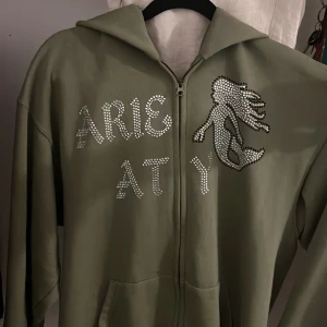 Rhinestone Hoodie (Arie Aty) - Tja, säljer nu min rhinestone hoodie som är i väldigt bra skick och bara använd förra sommaren. Har någon liten fläck på armen som går att tvätta bort. Skick 9/10. Storlek L men passar M då den suger åt sig bra vid tröjans hål.