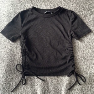 Svart t-shirt  - Svart t-shirt med knydetsljer på sidorna! Längden går att reglera och tröjan är väldigt skönt att ha på sig! Köparen står för frakten!