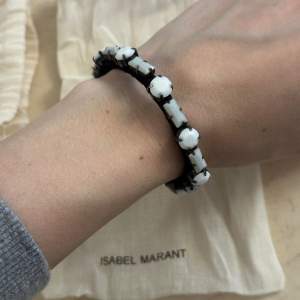 Oanvänt armband med vita stenar från Isabel Marant. Tillhörande smyckespåse ingår. Armbandets storlek justeras själv. 