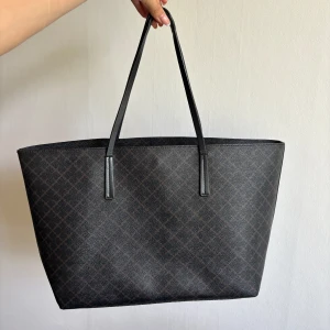 Malene Birger väska - Väska från Malene Birger i svart/brunt samt mellan storlek. Handtagen är slitna längst ut samt hörnen är slitna, samt fläck på baksidan av väskan (se bilder), därav det låga priset. Från framsidan ser den dock fortfarande fin ut! Dustbagen medkommer!