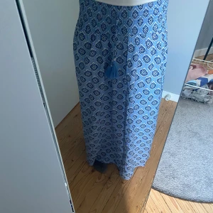 Blå långkjol - Säljer denna fina långkjol från Gina tricot. Säljer pga att den inte kommer till användning. Den är aldrig använd den har t.o.m kvar lappen. Det har låsnat några pärlor från en ”tofs” som man ser på bild 2 men det är inget man lägger märke till💗