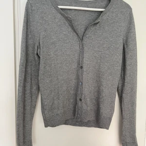 H&M grå cardigan M - Grå finstickad långärmad cardigan från H&M i fint skick. Strl M. 60 bomull, 40% polyester. Obs! Märkes och storlekslappar saknas.