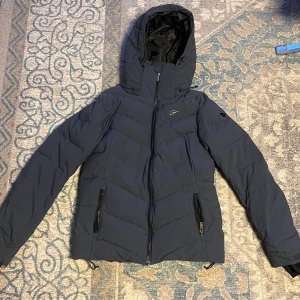 Skidjacka  - Mörkblå skidjacka som kan användas som vanlig jacka också. Den är ifrån five seasons och i topp skick. Den är i storlek 40 men passar mig som brukar ha 38.