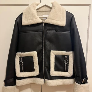 Svart pilotjacka   - Svart pilotjacka i fake läder med vita detaljer i teddymaterial. Från NA-KD i storlek 38.  Perfekt nu till våren. ⭐️
