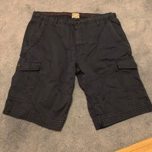 Cargoshorts  - Snygga mörkblåa cargoshorts i herrmodell från NEXT. Rak passform med fickor bak, fram och på sidorna.