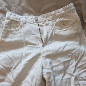 Vita cargo-jeans - Nästan helt oanvända, dvs mycket bra skick. Tre fickor på benen, och "vanliga" fickor upptill (inga bakfickor). Raka/vida ben, med kort slits längst ner så de lägger sig bra vid skorna.