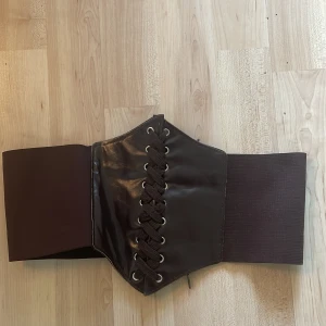 Korsettbälte - Säljer denna då den inte kommer till användning längre! Fakeläder med snörning fram och kardborreband bak, stretchig 