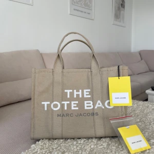 Marc Jacobs totebag - Säljer min fina marc Jacobs totebag. Självklart äkta. Alla lappar finns kvar. Köpt för 2500kr. Använd fåtal gånger. Lite smuts på undersidan av väskan som kommit av att den stått på marken (se bild 4) Ett långt svart over shoulder band medföljer.