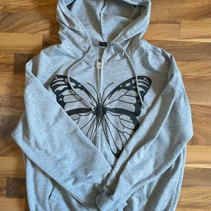 zip-up hoodie med tryck - fin hoodie från shein jag köpte här på plick. finns tecken att den använts men annars i bra skick. storlek M ljusgrå med fjärilstryck. hör av dig vid frågor :)