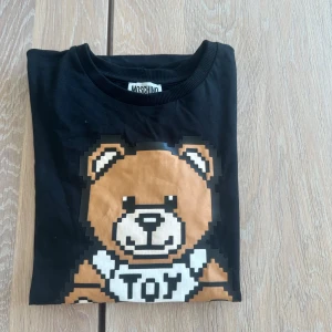  Moschino t shirt - Säljer nu denna  feta svarta t-shirten från Moschino med ett nalle tryck. är i strlk 170 och passar väll bäst till 170-175cm lång! är i nyskick då nästintill aldrig använd! köpt för 649kr och säljes för 349kr! hör av er vid intresse!🙌🏽🙌🏽