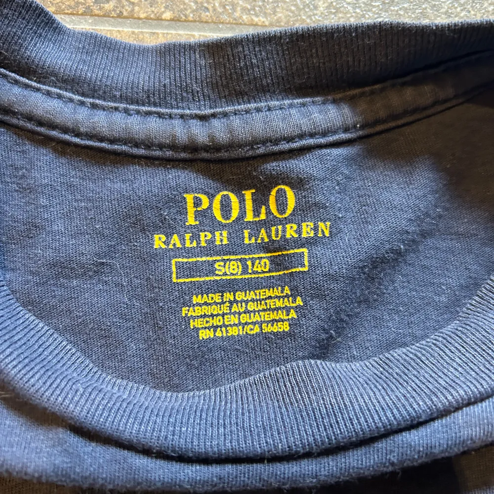 Säljer en mörkblå t-shirt från Polo Ralph Lauren med en cool amerikansk flagga på framsidan. Flaggan är lite sliten för en vintage look och har initialerna R.L. broderade i rött. T-shirten är i bomull och har korta ärmar. Perfekt för en casual look!. T-shirts.