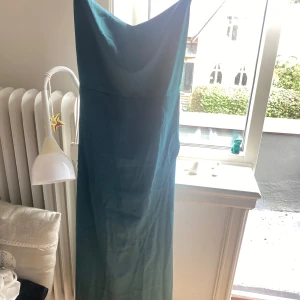 Blå långklänning med smala axelband - Säljer en elegant blå långklänning med smala axelband. Klänningen är tillverkad i ett glansigt material som ser ut som satin och har en figurnära passform. Perfekt för festliga tillfällen eller bal. Klänningen har en enkel men stilren design som gör den lätt att matcha med olika accessoarer.