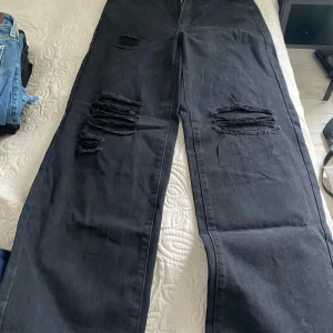 Svarta jeans med slitningar - Säljer ett par svarta jeans med coola slitningar på framsidan. De är i bra skick och har en avslappnad, baggy passform. Perfekta för en casual look! 🖤