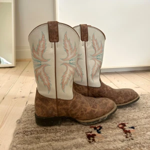 Bruna och vita cowboy boots - skitsnygga cowboy boots!! de har ett coolt broderat mönster i turkos och orange på skaftet. skorna är i äkta skinn och är köpta i texas. de är i bra skick! finns en fläck på backdelen av ena skon, skriv för mer bilder ❣️❣️