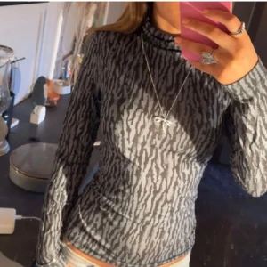 Långärmad tajt tröja med mönster  - Säljer en snygg grå och svart mönstrad polotröja. Den är långärmad och har ett coolt, nästan zebra-liknande mönster. Perfekt för höst och vinter! Tröjan är i bra skick och passar perfekt till både vardag och fest. 🖤
