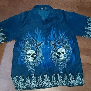 Banger blå skjorta med skallar🥶🥶 - Rkt sjuk blå skjorta med lite skallar och drakar och mönster🥶 några lösa trådar här och var, och en av knapparna är borta men annars i bra skick🙏 kom dm vid fler frågor😁🙏
