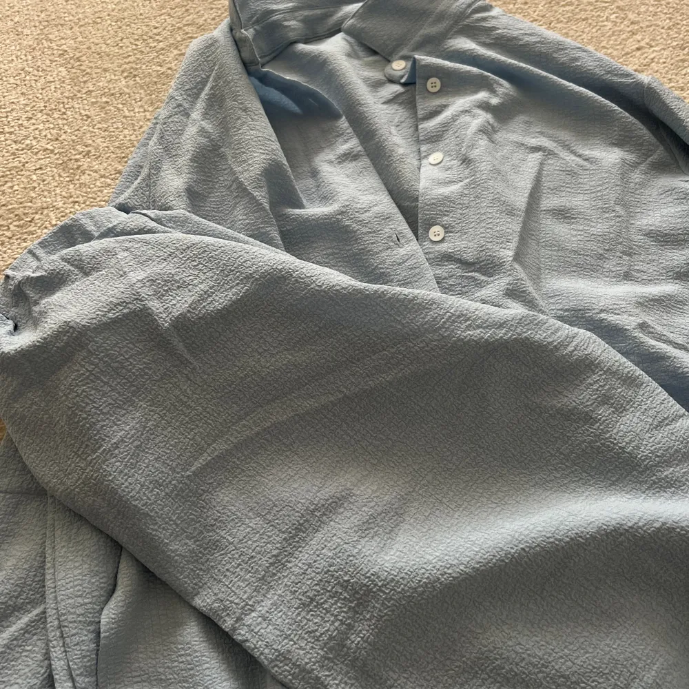 Ljusblått somrigt set med matchade skjorta och byxor.   Vita knappar längs med skjortan.   Endast använd 2-3 gånger, säljer pga att den blivit för liten.   Storlek XS med sitter mer som S då den är oversized.   Nypris: 329kr. Skjortor.